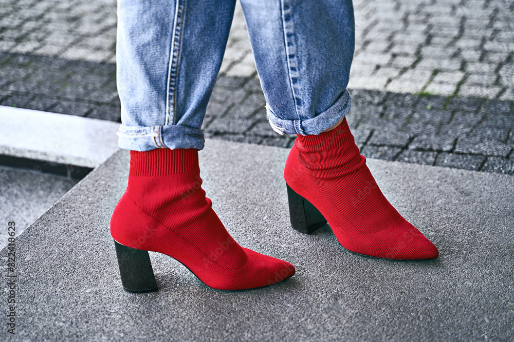 Woman legs in red sexy trendy stretch knitted fabric pointed toe block heel sock boots shoes and blue denim jeans pants