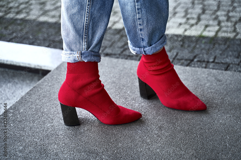 Woman legs in red sexy trendy stretch knitted fabric pointed toe block heel sock boots shoes and blue denim jeans pants