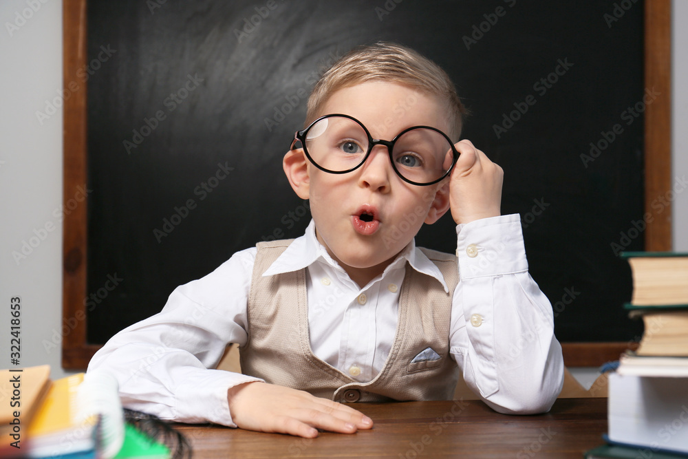 Cute little child wearing glasses at desk in classroom. First time at school Cute little child wearing glasses at desk in classroom. First time at school