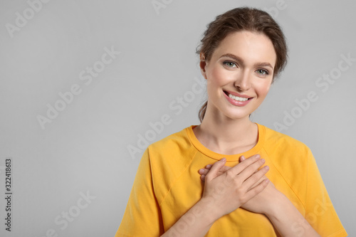 Beautiful grateful woman with hands on chest against light grey background. Space for text