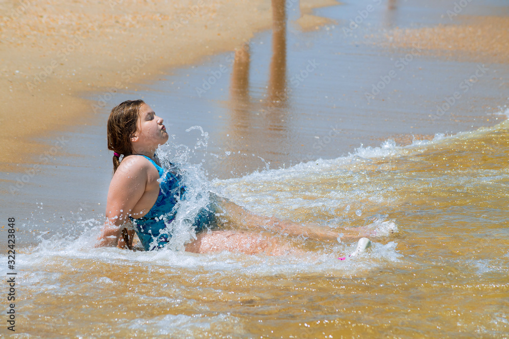 Cute girl in a blue swimsuit sitting on the sand in waves on the beach. Cute girl in a blue swimsuit sitting on the sand in waves on the beach.