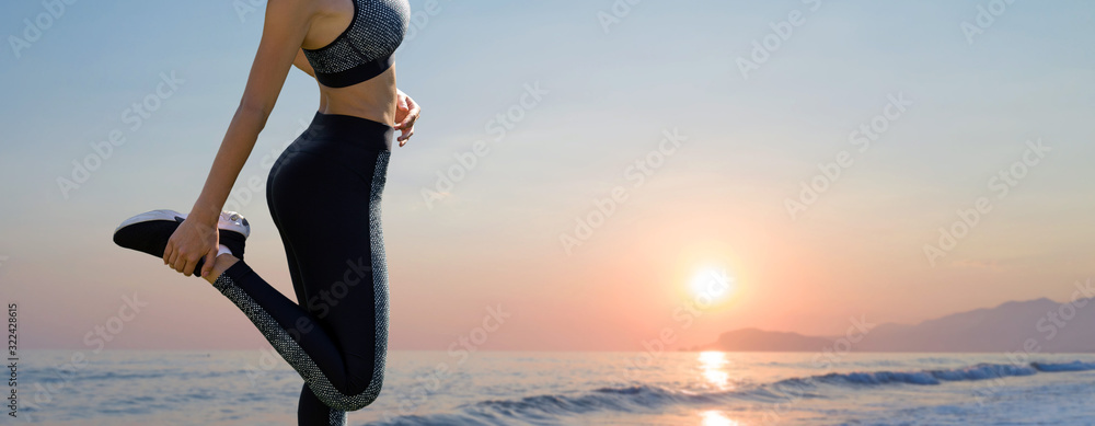 Fototapeta premium A thin athletic girl takes a break between classes on the background of the sunset by the sea in the early morning, enjoys silence and freedom.