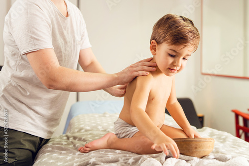 Small caucasian boy in underwear naked sitting on the therapeutic massage bed at hospital or salon while doctor therapist nurse exam or treatment Physiotherapist back massage professional