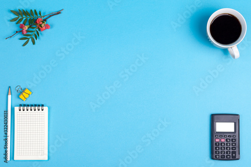 Flat lay of minimal workspace desk with notebook , pencil, calculator, coffee and green plant copy space on blue tone