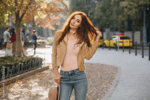 Shapely caucasian lady playing with her long red hair in october day. Outdoor shot of sensual ginger female model relaxing in september morning.