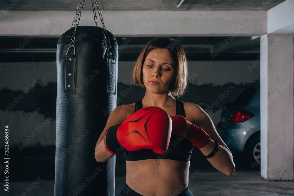 Confident young woman putting on her red boxing gloves