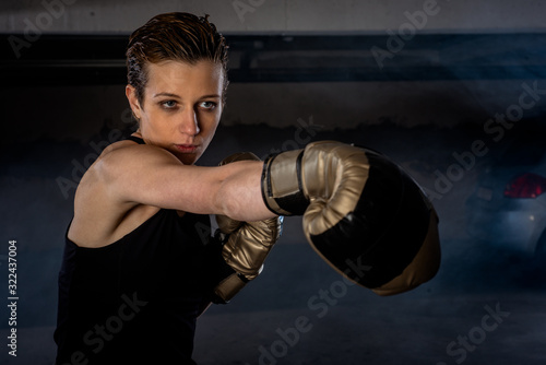 Closeup picture of beautiful female boxer practicing her punches with gold boxing gloves © qunica.com
