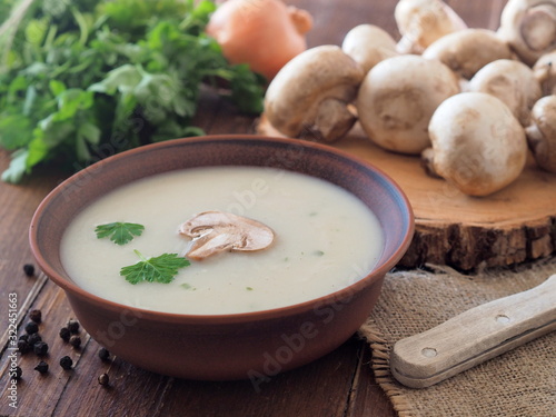 French mushroom soup and ingredients - fresh mushrooms and green herbs on a wooden table.