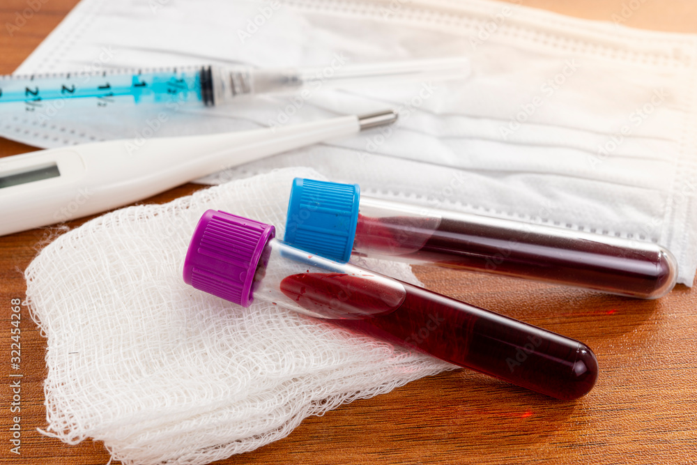 Tube with blood for examination with injection, thermometer and mask for exams. Wooden table background. Tube with blood for examination with injection, thermometer and mask for exams. Wooden table background.