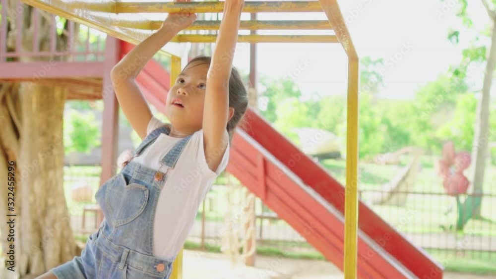 Asian little girl is enjoying activity in a hanging bar by her hand at outdoors playground. Slow motion. Asian little girl is enjoying activity in a hanging bar by her hand at outdoors playground. Slow motion.