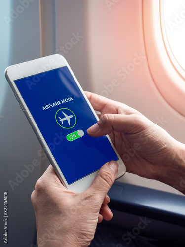 Flight mode concept. Hand holding white smartphone and turned on airplane mode on screen near the window on the airplane. photo