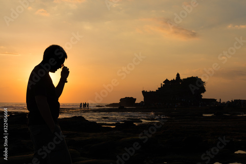 A man take of sun glasses in silhouette look at Pura Tanah lot, Bali, Indonesia.