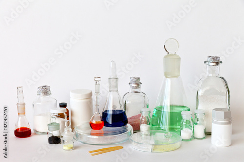 Chemical laboratory, reagents, solutions in flasks, salts in jars and powders in Petri dishes on a laboratory table. The concept of chemical research. White background, place for text