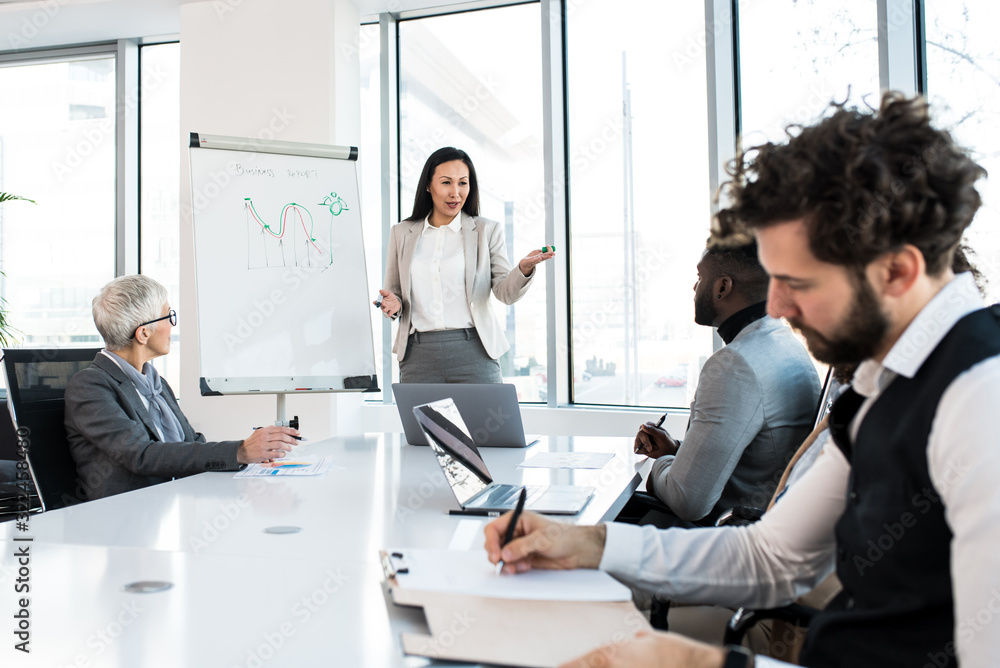 © Sanja - A young competent analyst presenting a graph to the company's team at the conference room.