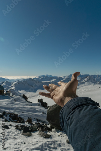 Male open hand showing at snowy Caucasus mountain range landscape at Elbrus mountain on sunny day. Hiking travel concept. 