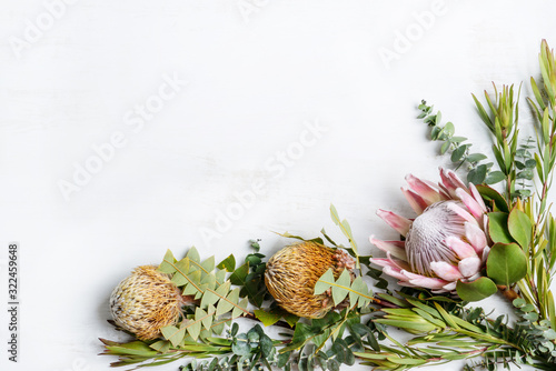 Beautiful floral arrangement of a pink King Protea and yellow/orange banksias surrounded by leucadendrons and Australian eucalyptus leaves creating a floral border on a white background.