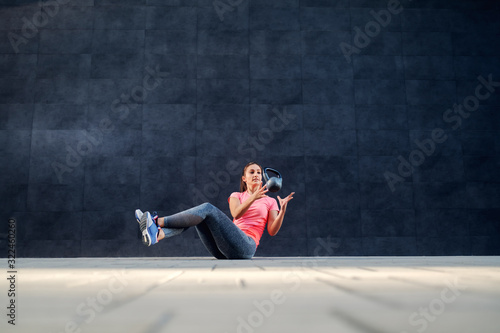 Fit dedicated strong brunette in sportswear doing russian twist exercise with kettle bell.