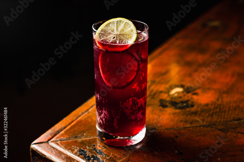 A red cocktail in a highball glass garnished with lime wheels