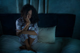 dramatic night lifestyle portrait of young sad and depressed middle eastern woman with curly hair sleepless in bed awake and thoughtful feeling worried suffering depression