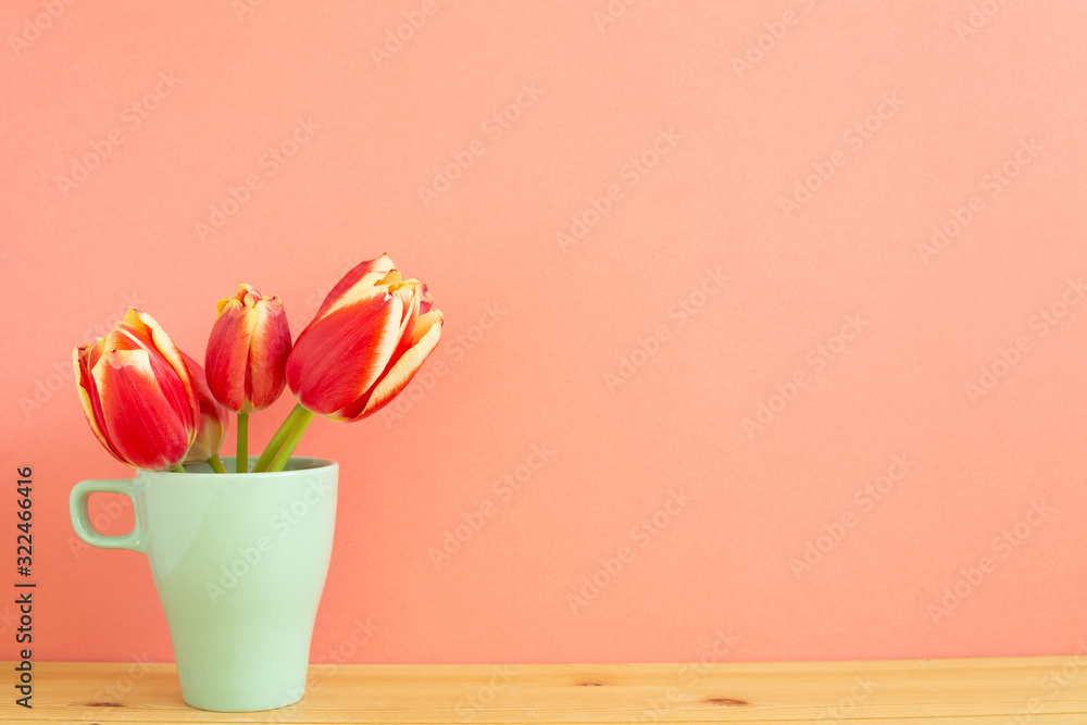 Obraz premium Red tulip flowers on wooden table with orange background. Spring floral arrangement, copy space