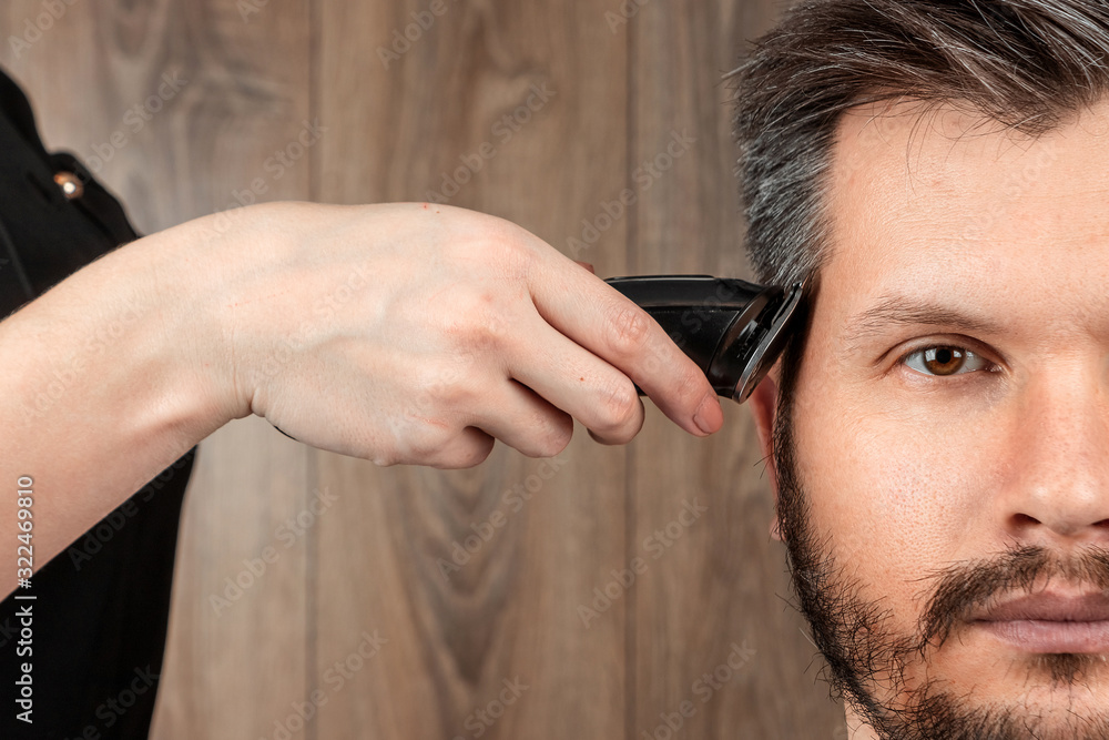 Obraz premium The master makes a haircut to the client with an electric machine, trimmer, close-up. The process of male haircuts at the hairdresser, barbershop. Body care, lifestyle, metrosexual.
