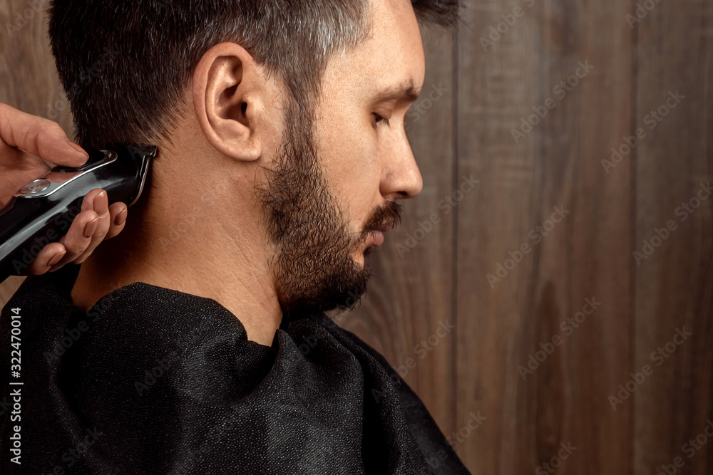 Obraz premium The master makes a haircut to the client with an electric machine, trimmer, close-up. The process of male haircuts at the hairdresser, barbershop. Body care, lifestyle, metrosexual.
