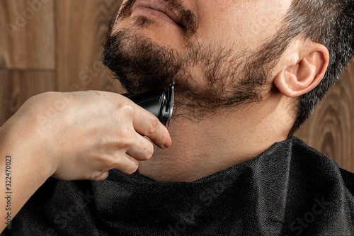 The master makes a beard haircut to the client with an electric machine, trimmer, close-up. The process of shaving a beard at the hairdresser. Body care, lifestyle, metrosexual.