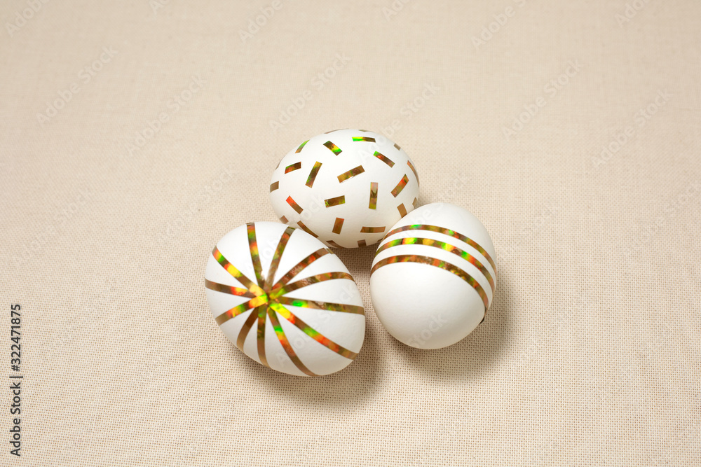 Three Creative golden Easter eggs on Natural fabric background.
