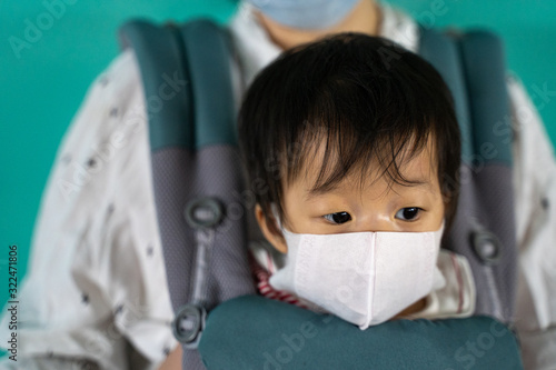 Asian baby with mother in baby carry,baby is wearing a protection mask against air pollution and Wuhan covic-19 corona virus before flight in terminal DonMuang airport,Bangkok, Thailand. photo