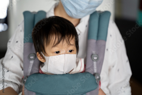 Asian baby with mother in baby carry,baby is wearing a protection mask against air pollution and Wuhan covic corona virus before flight in terminal DonMuang airport,Bangkok, Thailand. photo