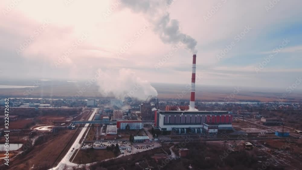 Aerial shot Pipes with smoke: industrial production, plant, air pollution. Dense thick smoke comes from industrial red-white pipes: from a bird's eye view. Industrial zone: smoke comes from the pipe