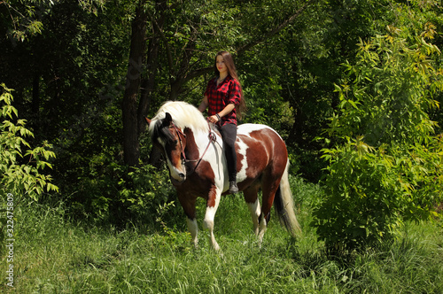 Beautiful country girl bareback ride her painted tinker horse in woods glade at sunset