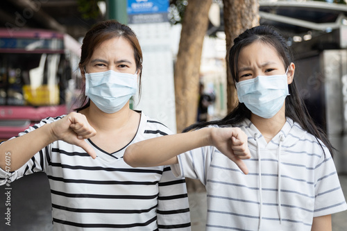 Asian child girl,woman show thumbs down,wearing medical face mask in public area,risk of disease,bad air pollution,hard to breathe,epidemic,spread of Coronavirus,2019-nCoV,MERS-CoV,Wuhan,flu season