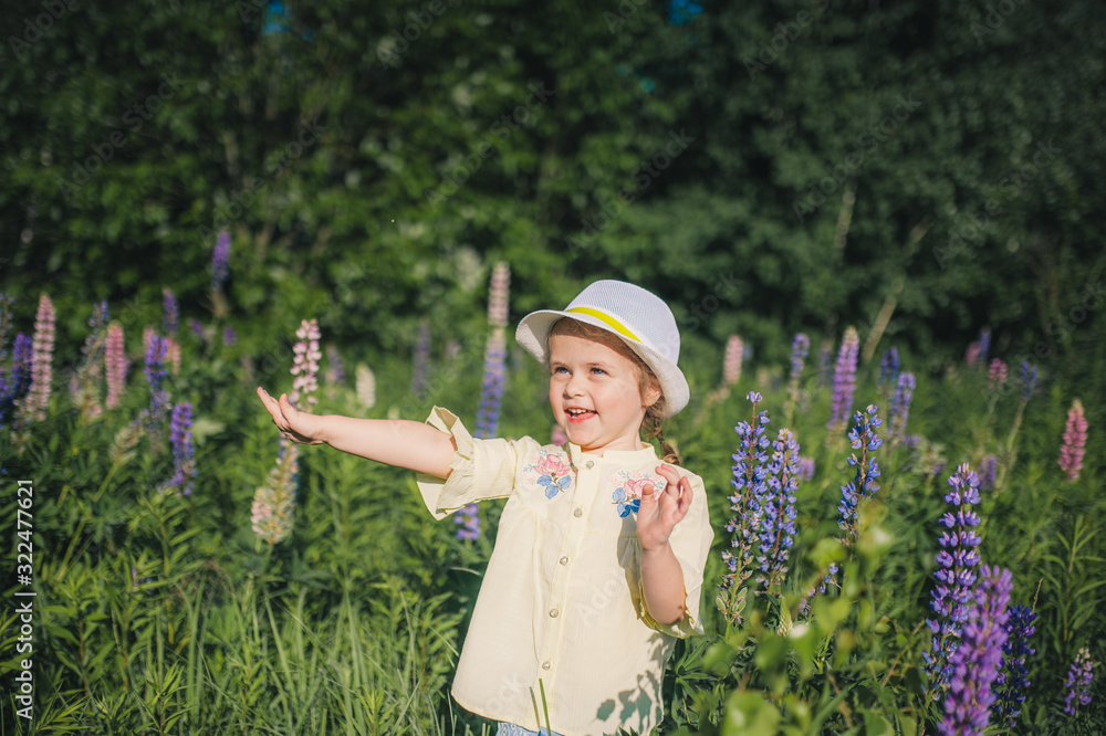 Portrait of a little girl in a hat in a field of flowers. Field of Lupins. Summer
