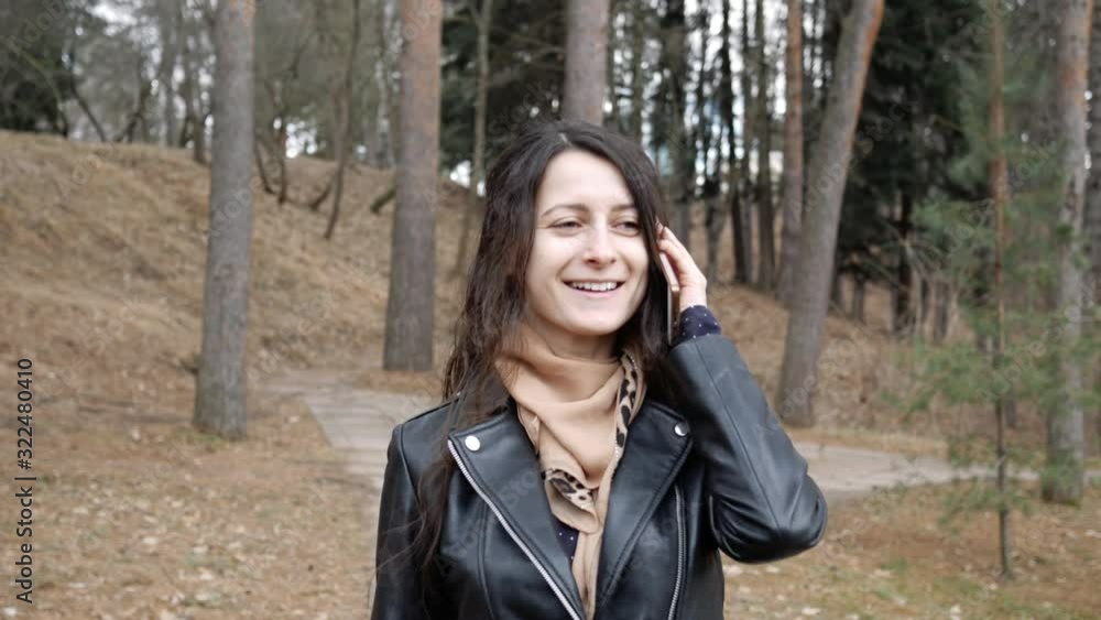 Beautiful young cheerful woman wearing in leather jacket walking in autumn park, talking on mobile phone. She glad to hear caller Beautiful young cheerful woman wearing in leather jacket walking in autumn park, talking on mobile phone. She glad to hear caller