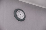 Round clock hanging on gray wall indoors.