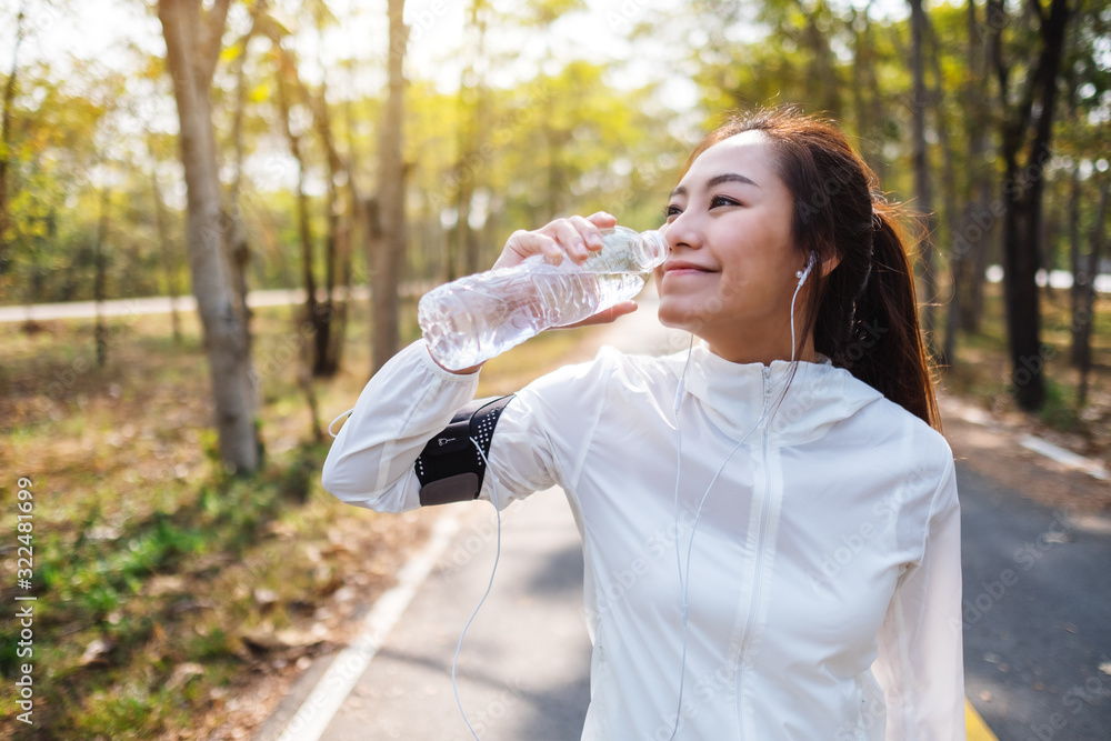 Closeup image of an asian female runner drinking water from bottle after jogging in city park