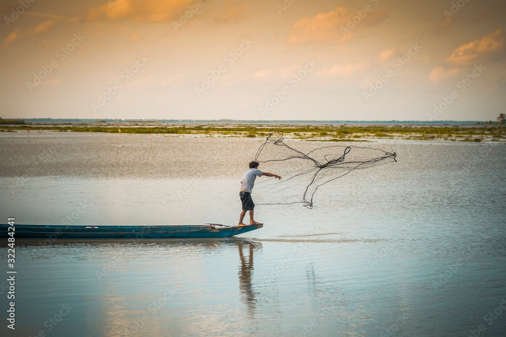 Fisherman standing on a wooden boat sowing nets Fisherman standing on a wooden boat sowing nets