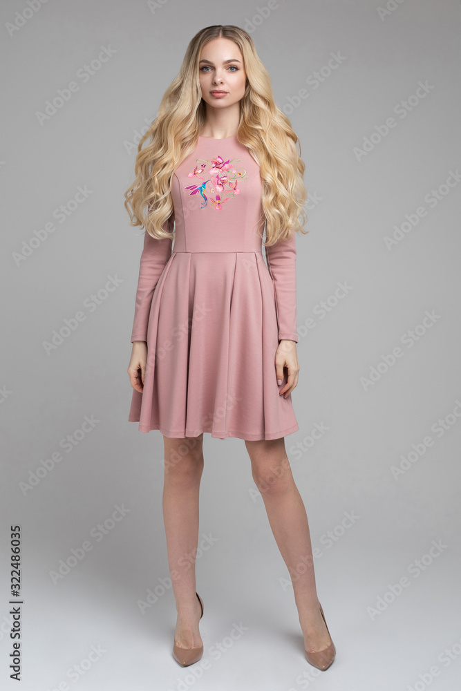 Stock photo studio portrait of an attractive blonde young adult woman with wavy hair wearing lovely pink dress with print on top. She is looking at camera tenderly. Stock photo studio portrait of an attractive blonde young adult woman with wavy hair wearing lovely pink dress with print on top. She is looking at camera tenderly.