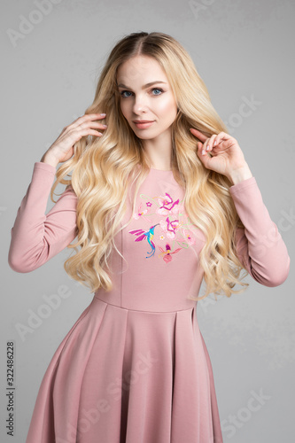 Stock photo studio portrait of an attractive blonde young adult woman with wavy hair wearing lovely pink dress with print on top. She is looking at camera tenderly.