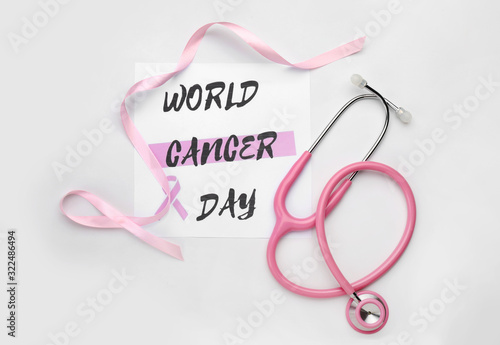 Pink ribbon, stethoscope and paper sheet with text WORLD CANCER DAY on white background