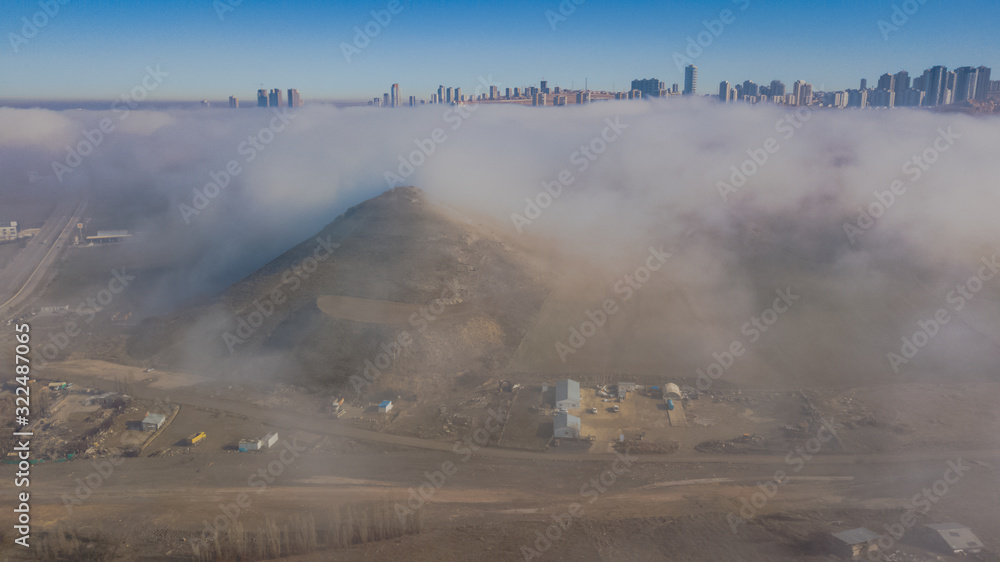 Landscape over the clouds in foggy weather. Hills of buildings in foggy weather. The drone and the top of the fog layer. Buildings in the fog.