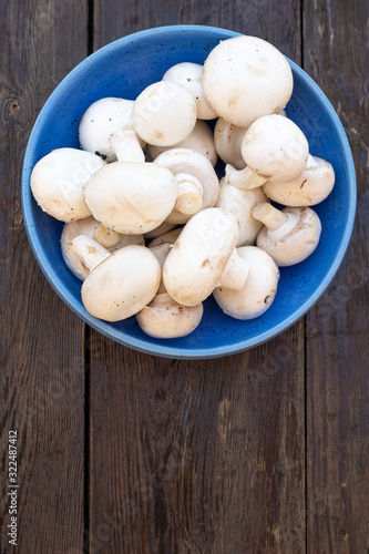 Fresh white Champignon mushrooms on vintage wood table background. In a blue bowl