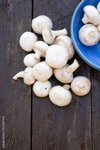 Fresh white Champignon mushrooms on vintage wood table background. In a blue bowl