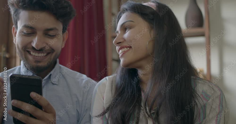 Indian couple discuss and buy online together as they share their smart phone mobile phone using their bank debit cards and celebrate with high five their hands, slow-motion handheld 60 fps