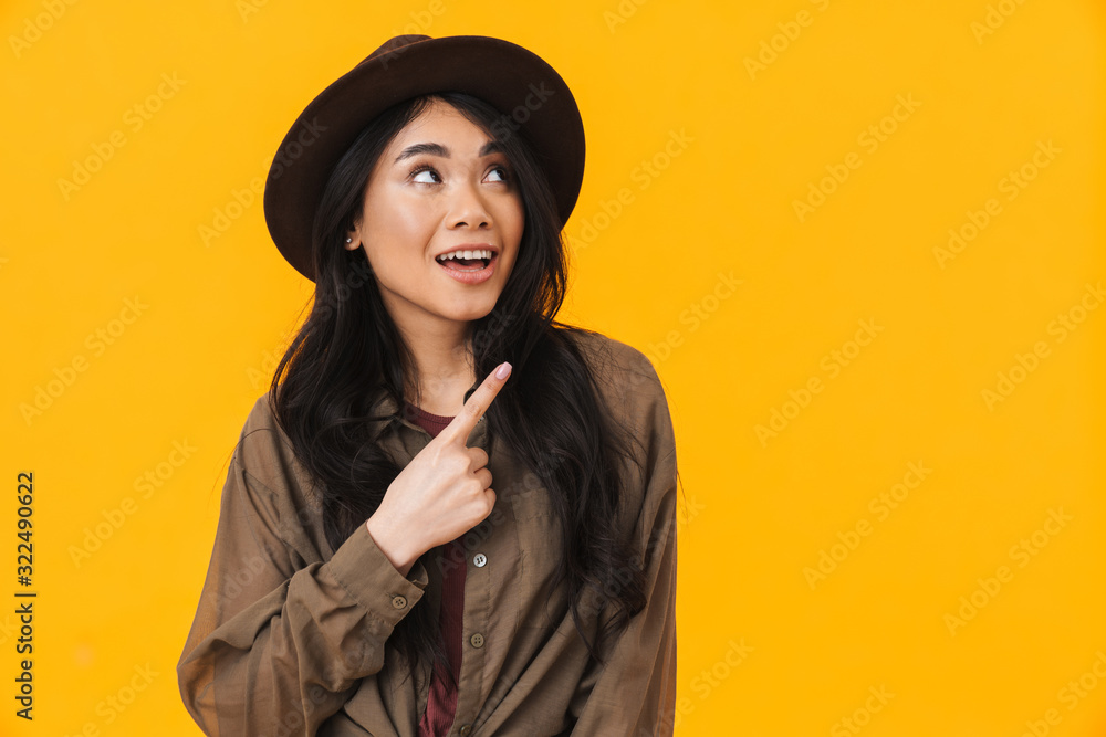 Image of young asian woman wearing hat smiling and pointing finger Image of young asian woman wearing hat smiling and pointing finger