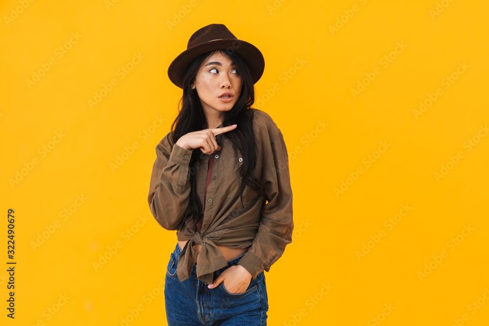 Image of young asian woman wearing hat smiling and pointing finger Image of young asian woman wearing hat smiling and pointing finger