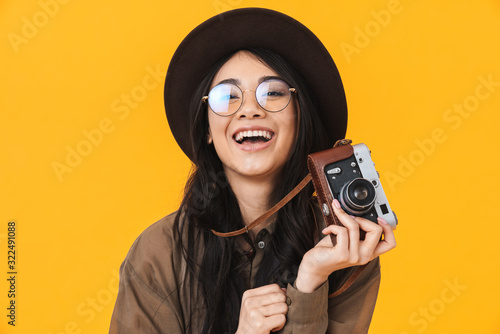 Image of brunette asian tourist woman wearing hat using retro camera
