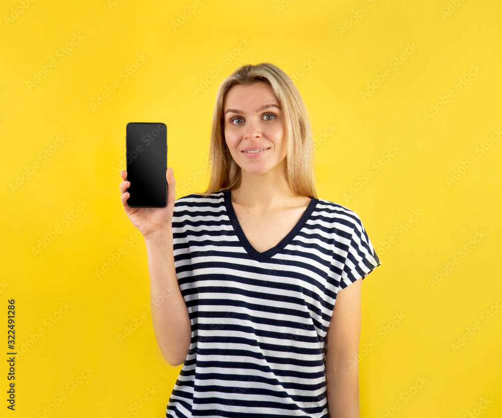 Naklejka premium Joyful woman demonstrating smartphone blank display screen to camera on yellow background. Copy space for your promo