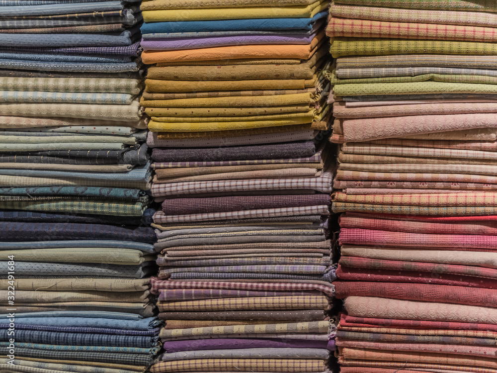 Fabric scarves and shawls of different colors, textures and patterns are stacked in vertical stacks. Background image.
